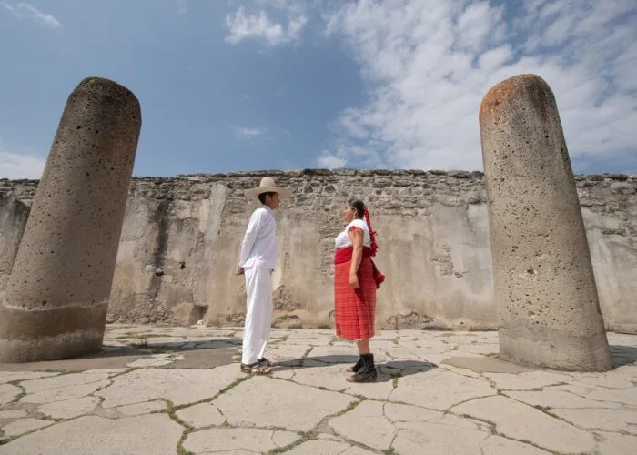 Zapotec couple in traditional dress between ancient stone columns at the Mitla archaeological site in Oaxaca