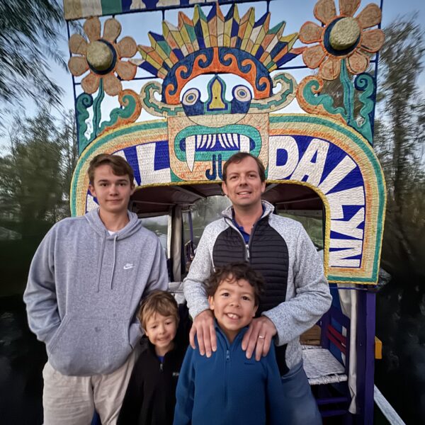 Family posing in front of a colorful trajinera archway during a Xochimilco sunrise tour in Mexico City by Mexico Foodie Tours