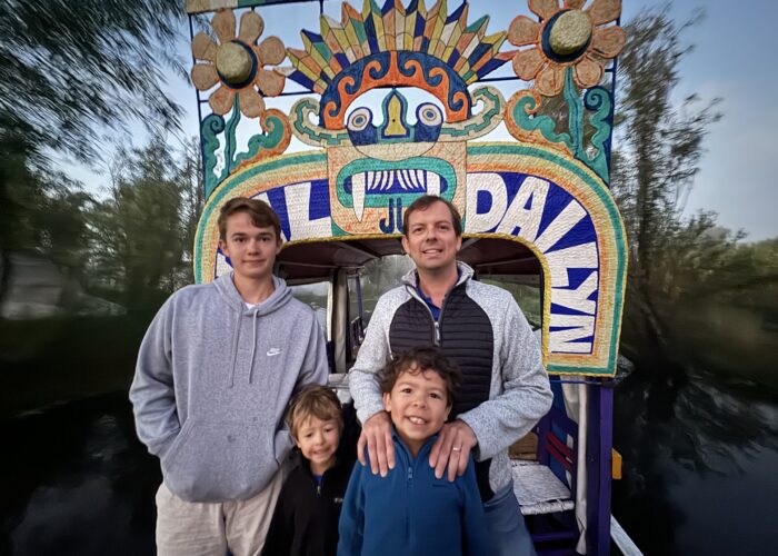 Family posing in front of a colorful trajinera archway during a Xochimilco sunrise tour in Mexico City by Mexico Foodie Tours