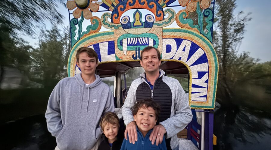 Family posing in front of a colorful trajinera archway during a Xochimilco sunrise tour in Mexico City by Mexico Foodie Tours