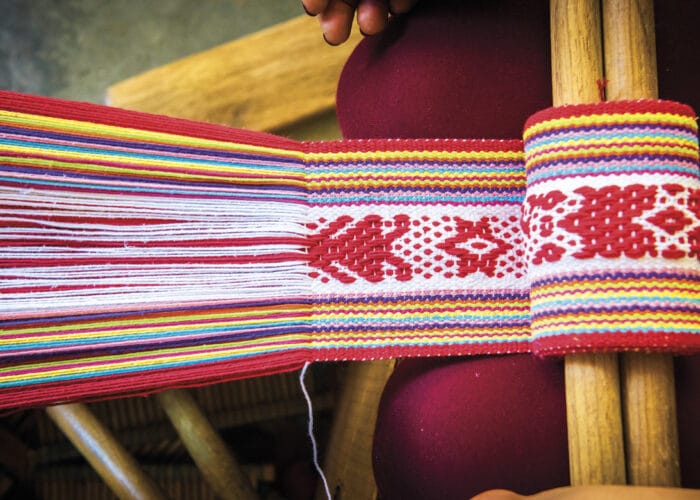 A close-up of colorful woven fabric with intricate patterns being made on a traditional backstrap loom, often seen along the routes of Authentic food tours and Mexico Foodie Tours for a rich cultural and culinary experience.