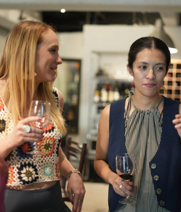 Three women stand indoors holding wine glasses, engaged in conversation near a wine fridge. Bottles and shelves line the background, capturing a moment that feels like an authentic food tour inspired by Mexico Foodie Tours. Three women stand indoors holding wine glasses, engaged in conversation near a wine fridge. Bottles and shelves line the background, capturing a moment that feels like an authentic food tour inspired by Mexico Foodie Tours.