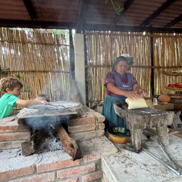 Traditional cook shaping masa on a metate beside a wood-fired comal during an Oaxaca cooking class by Mexico Foodie Tours