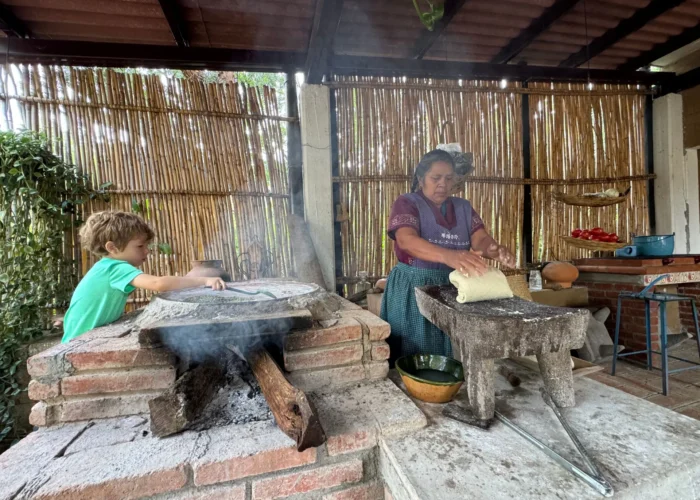 Traditional cook shaping masa on a metate beside a wood-fired comal during an Oaxaca cooking class by Mexico Foodie Tours