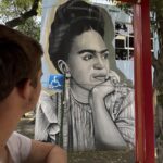 Tour guest viewing a black-and-white Frida Kahlo street mural in Coyoacán, Mexico City, during a Mexico Foodie Tours walking tour