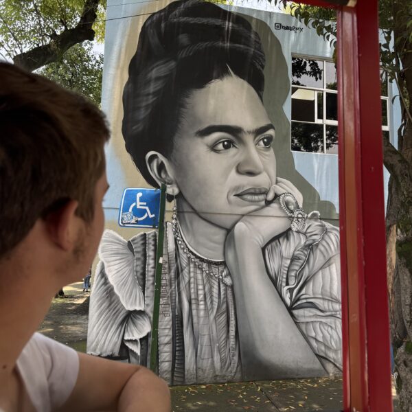 Tour guest viewing a black-and-white Frida Kahlo street mural in Coyoacán, Mexico City, during a Mexico Foodie Tours walking tour