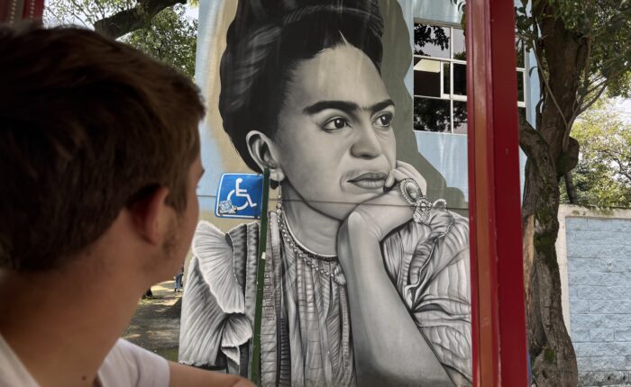 Tour guest viewing a black-and-white Frida Kahlo street mural in Coyoacán, Mexico City, during a Mexico Foodie Tours walking tour