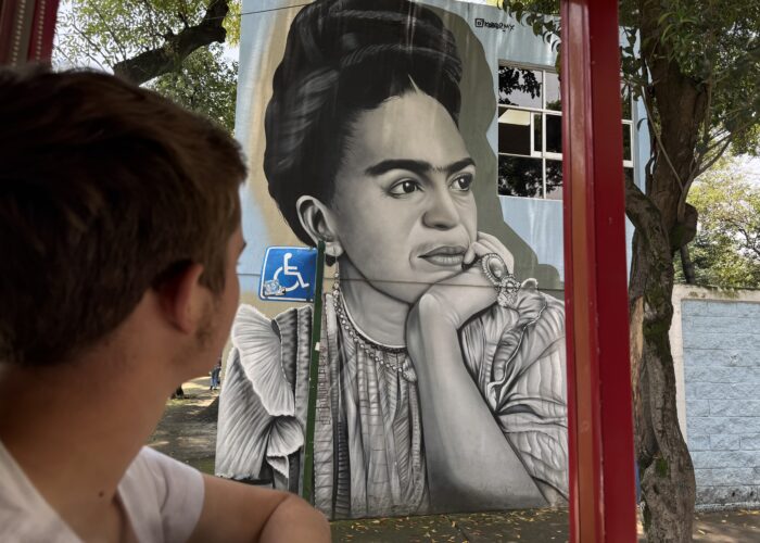 Tour guest viewing a black-and-white Frida Kahlo street mural in Coyoacán, Mexico City, during a Mexico Foodie Tours walking tour