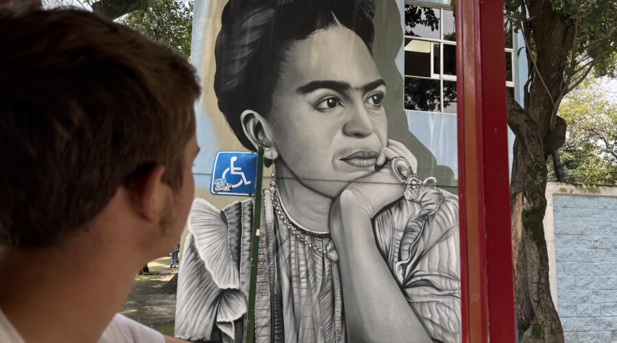 Tour guest viewing a black-and-white Frida Kahlo street mural in Coyoacán, Mexico City, during a Mexico Foodie Tours walking tour