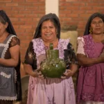 Three Oaxacan women artisans holding handmade clay pottery, including green glazed Atzompa ceramics, on an Oaxaca artisan tour by Mexico Foodie Tours