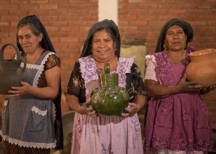 Three Oaxacan women artisans holding handmade clay pottery, including green glazed Atzompa ceramics, on an Oaxaca artisan tour by Mexico Foodie Tours