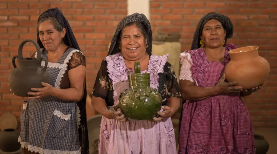 Three Oaxacan women artisans holding handmade clay pottery, including green glazed Atzompa ceramics, on an Oaxaca artisan tour by Mexico Foodie Tours