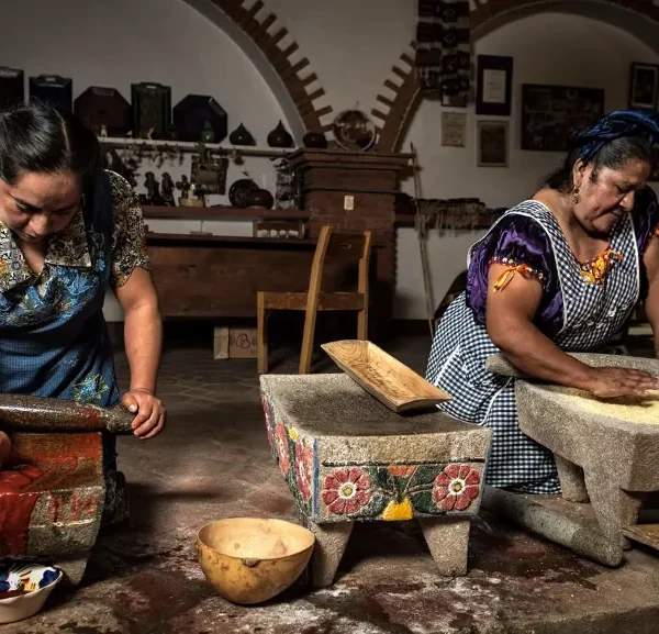 Two traditional women cooks part of Círculos de Sabor, grinding maize and chiles on stone metates in Mexico.