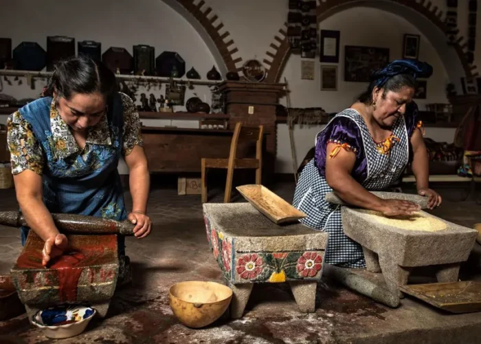 Two traditional women cooks part of Círculos de Sabor, grinding maize and chiles on stone metates in Mexico.