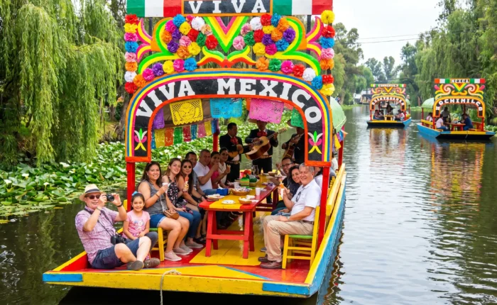 Colorful trajinera decorated with flowers and papel picado gliding through the canals on the Xochimilco Tour by Mexico Foodie Tours, with mariachi musicians and guests aboard.