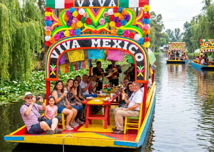 Colorful trajinera decorated with flowers and papel picado gliding through the canals on the Xochimilco Tour by Mexico Foodie Tours, with mariachi musicians and guests aboard.
