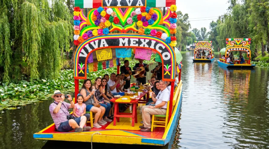 Colorful trajinera decorated with flowers and papel picado gliding through the canals on the Xochimilco Tour by Mexico Foodie Tours, with mariachi musicians and guests aboard.