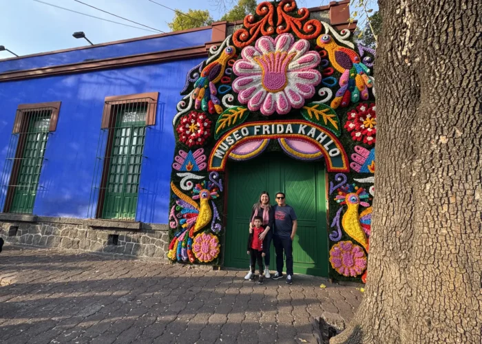 Family posing at the Museo Frida Kahlo Casa Azul entrance during a Coyoacán food tour in Mexico City by Mexico Foodie Tours
