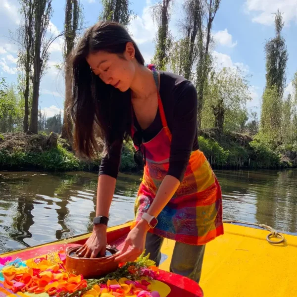 Traveler preparing food in a clay cazuela aboard a flower-decked trajinera in Xochimilco on one of our food tours in Mexico City