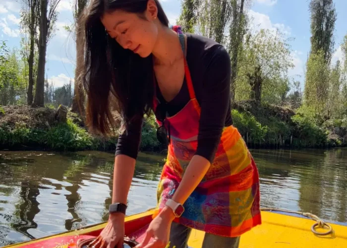 Traveler preparing food in a clay cazuela aboard a flower-decked trajinera in Xochimilco on one of our food tours in Mexico City